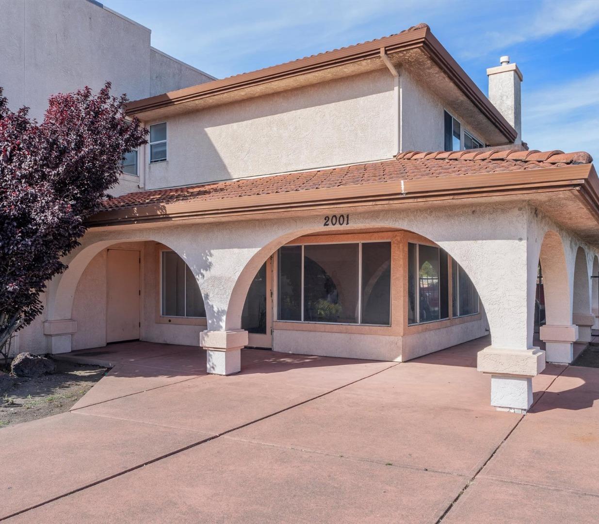 Two-story stucco property with terracotta roofs, arched entrance, and paved forecourt.