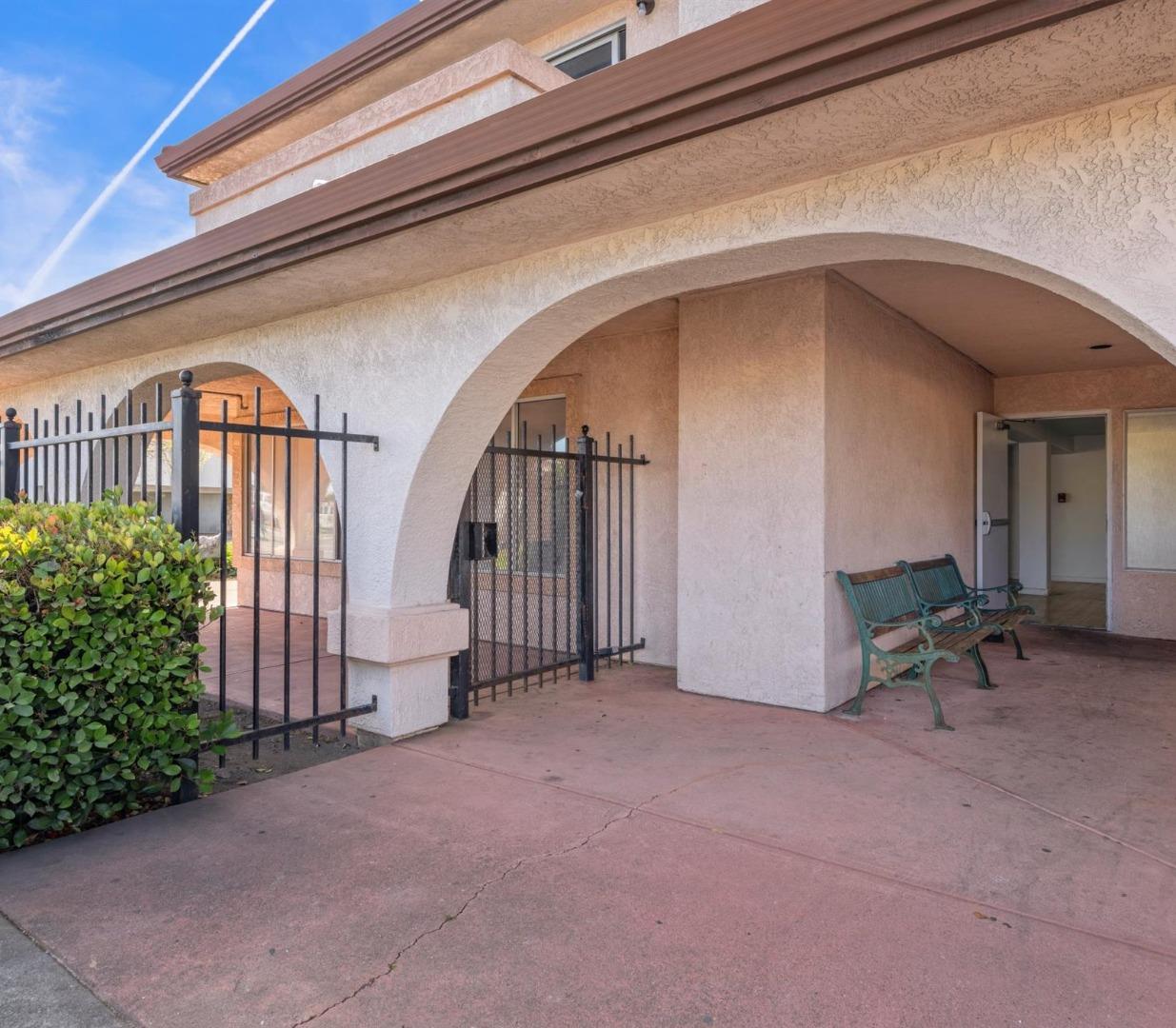 Stucco building entrance with arched entryways, black metal gates, and green benches.