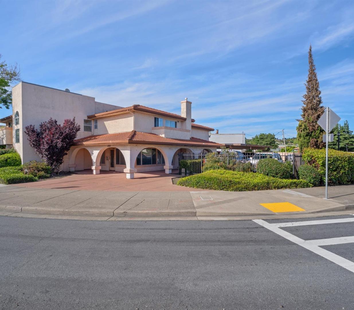 Two-story stucco building with an arched entry, red tile roof, and gated parking.