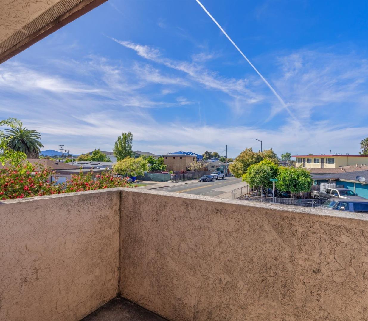 Balcony overlooking a residential street and distant hills beneath a blue sky.