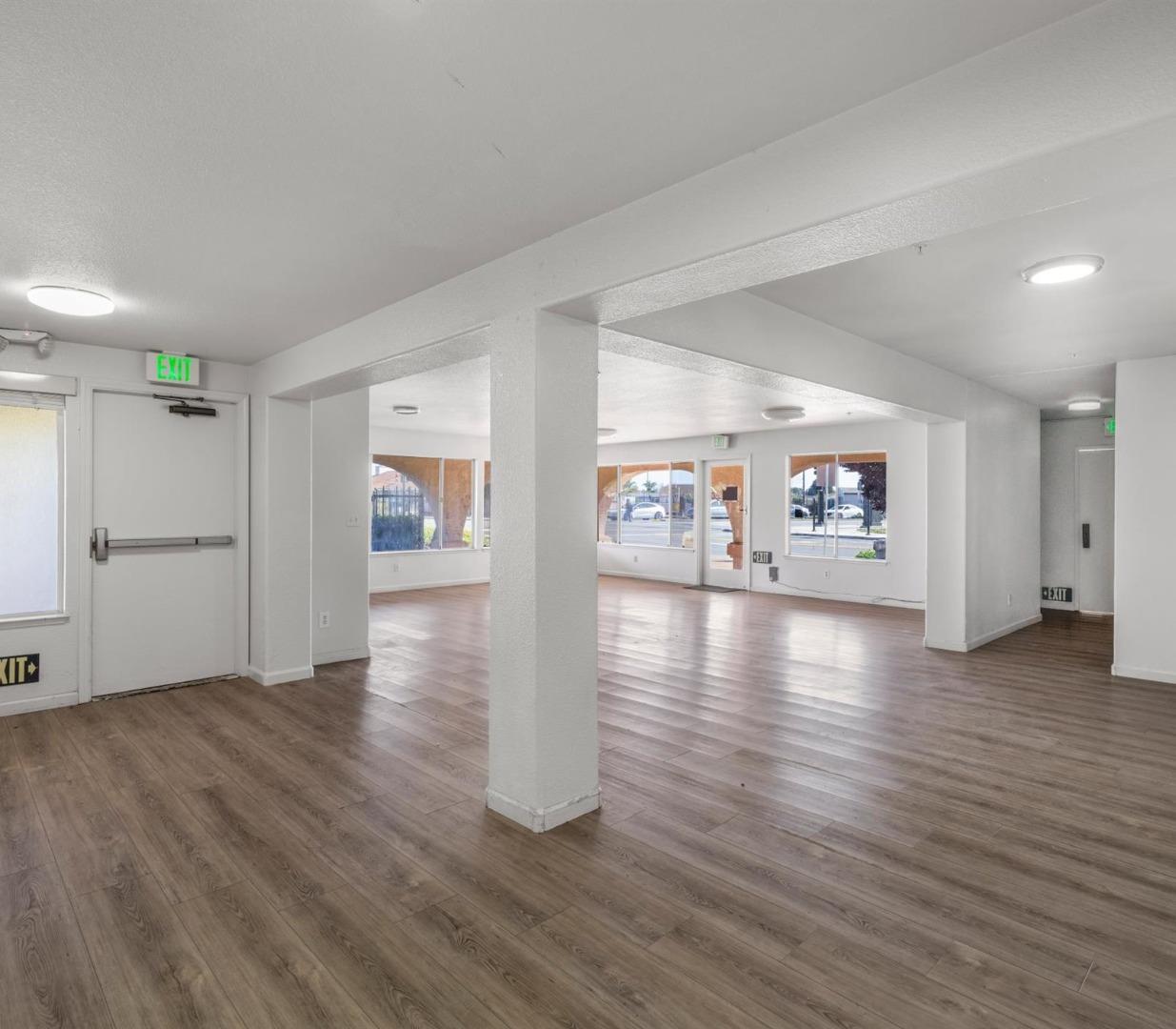 Vacant open commercial space with wood-look flooring, a central column, and large street-facing windows.
