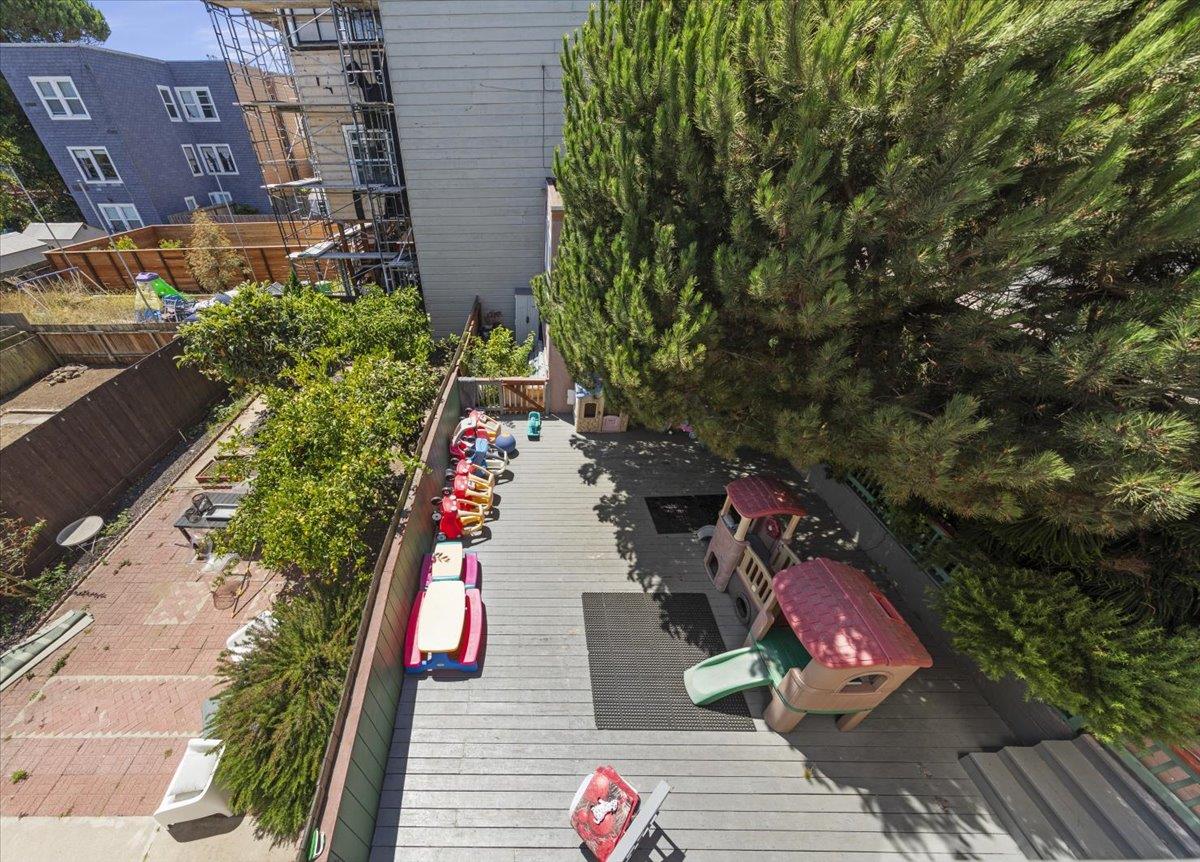 Fenced backyard with a gray deck, children’s play equipment, and a large evergreen tree.