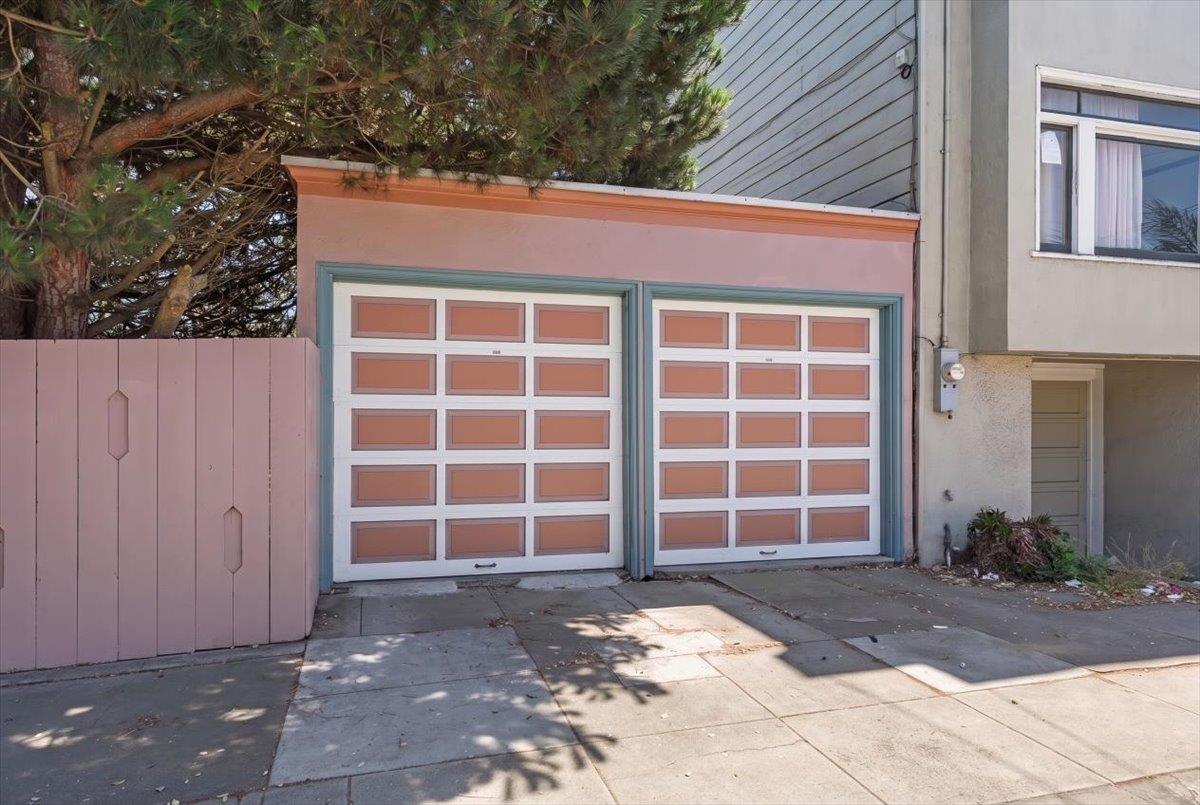 Two pink-paneled garage doors with blue-green trim beneath a large tree.