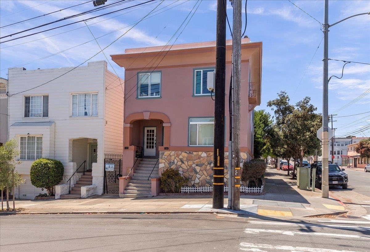 Pink multi-story residential building with a stone-clad base and front steps on a San Francisco street.