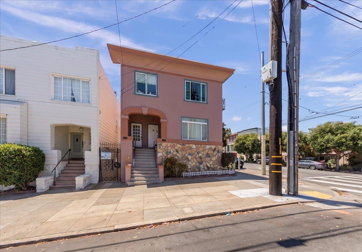 Pink two-story residence with a stone-patterned facade and broad roof overhang at a sunny street corner.