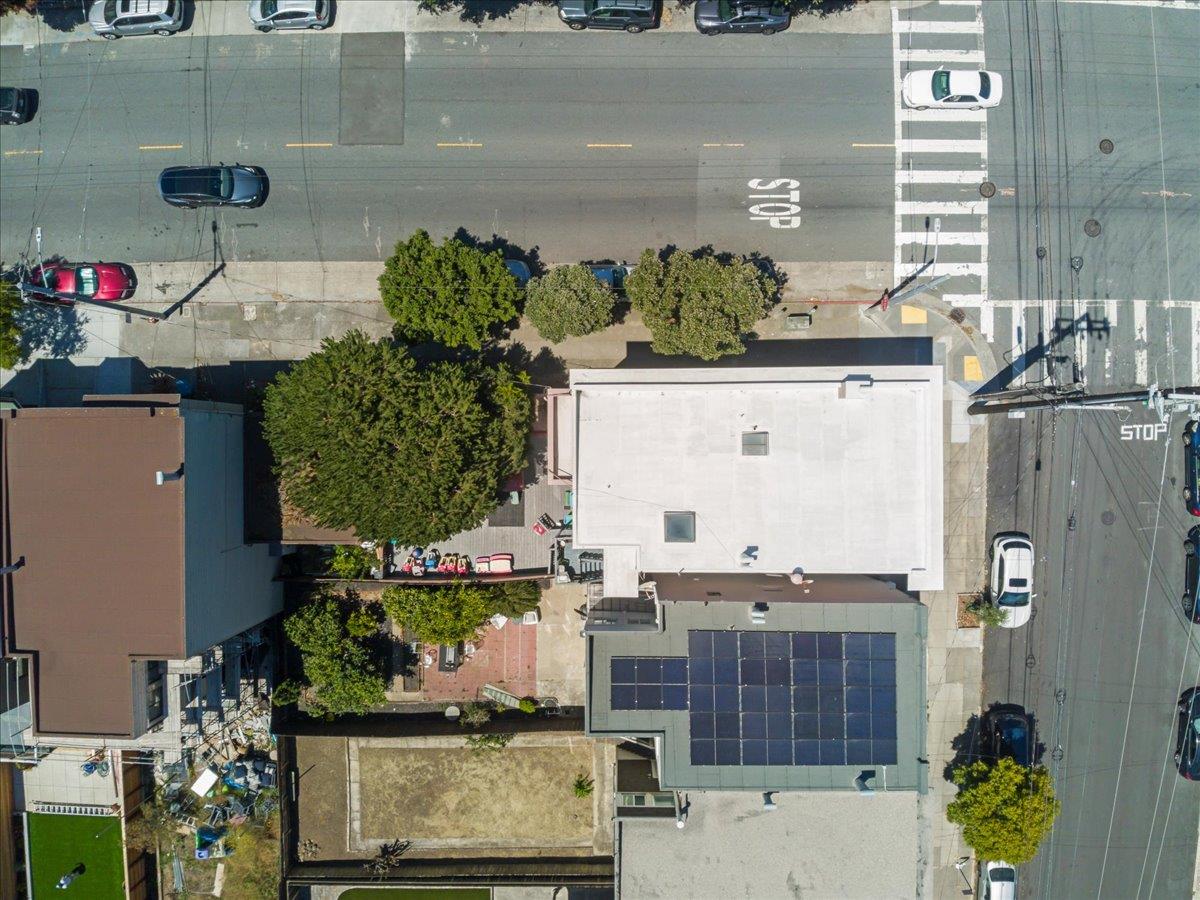 Aerial view of a white flat-roofed building at a San Francisco intersection, surrounded by trees and neighboring rooftops.
