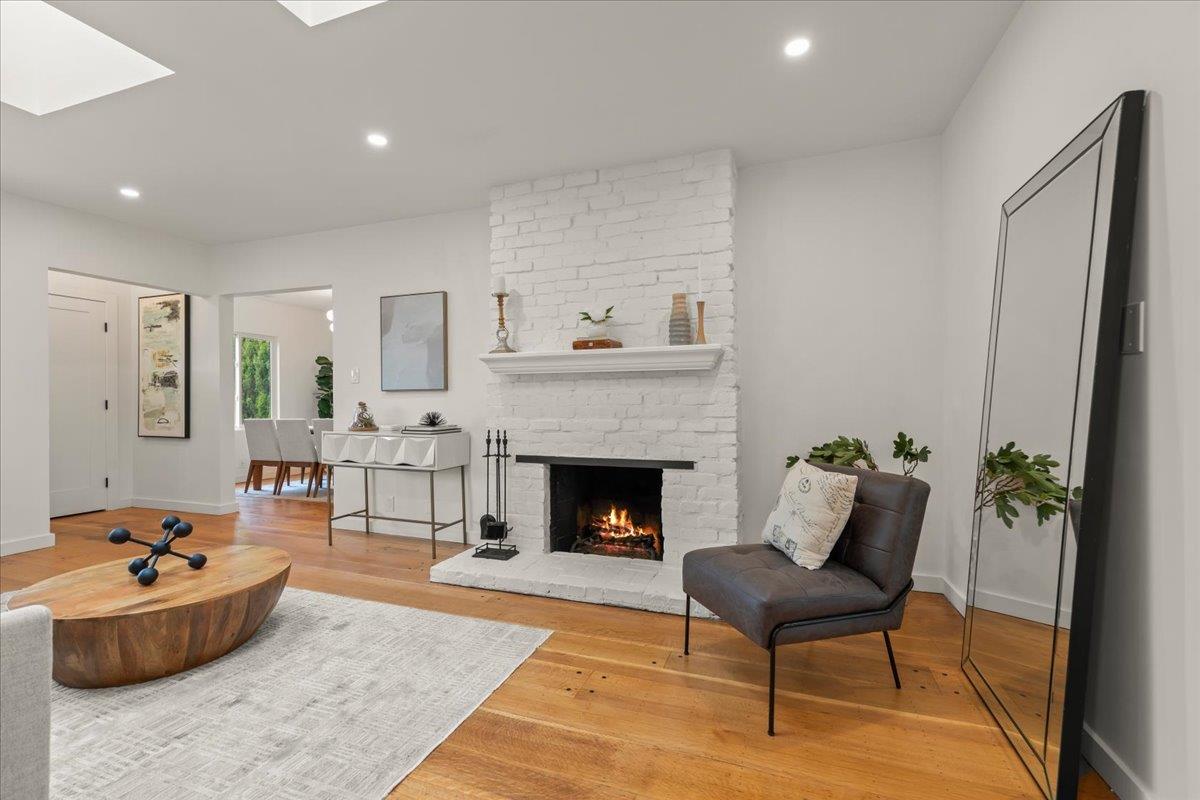 Living room with a white brick fireplace, hardwood floors, and a round wood coffee table.