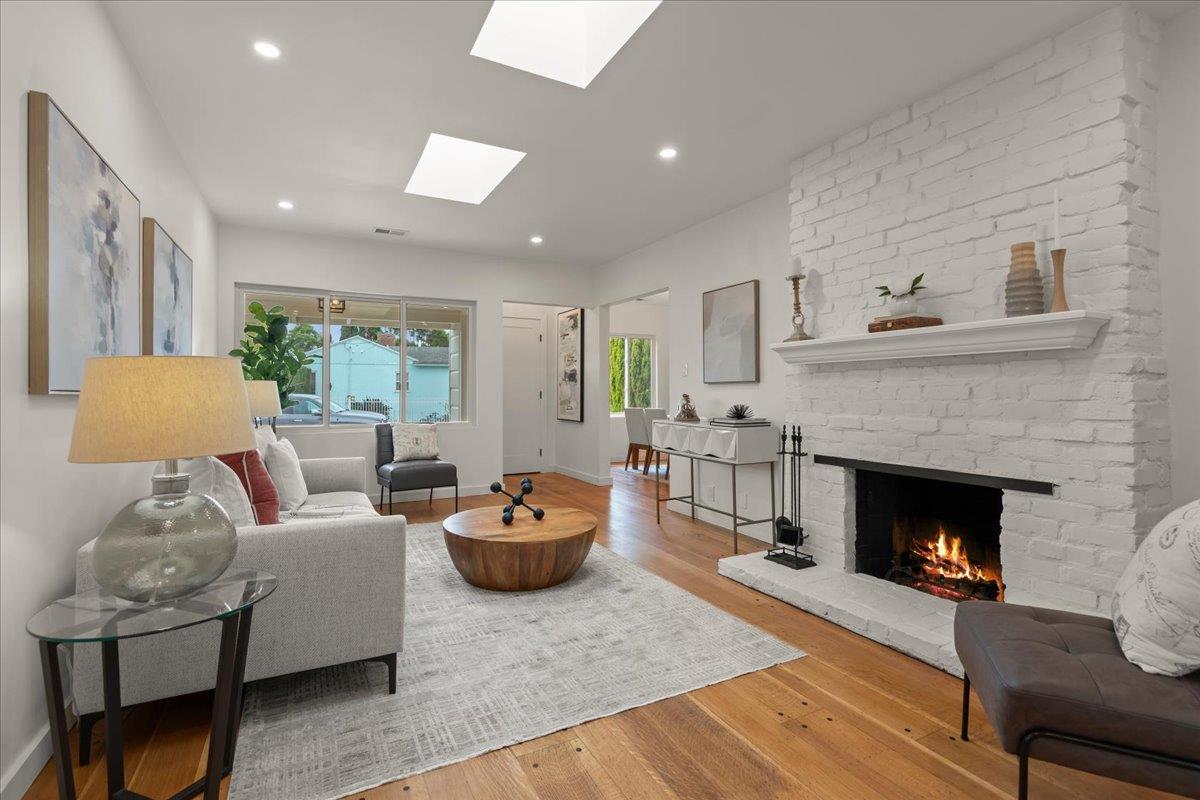 Staged living room with a white brick fireplace, hardwood floors, and large windows.