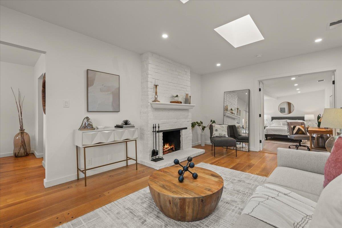 Living room with a white brick fireplace, hardwood floors, and an open bedroom doorway.