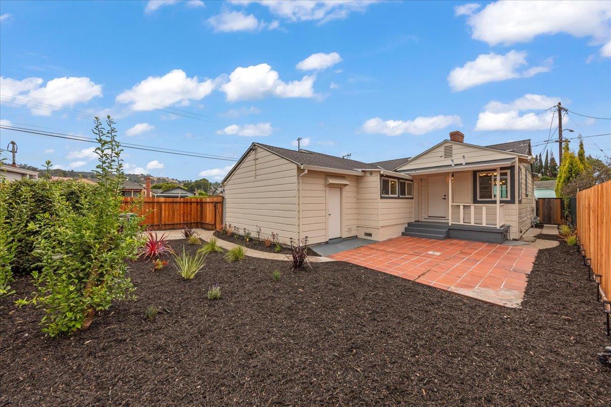 Rear of a beige single-story house with a terracotta patio and landscaped fenced yard.