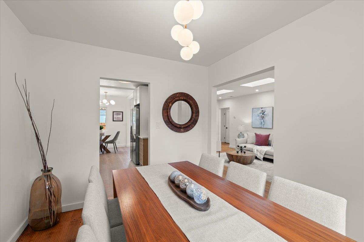Dining room with a long wood table and sculptural pendant, opening to the kitchen and living room.