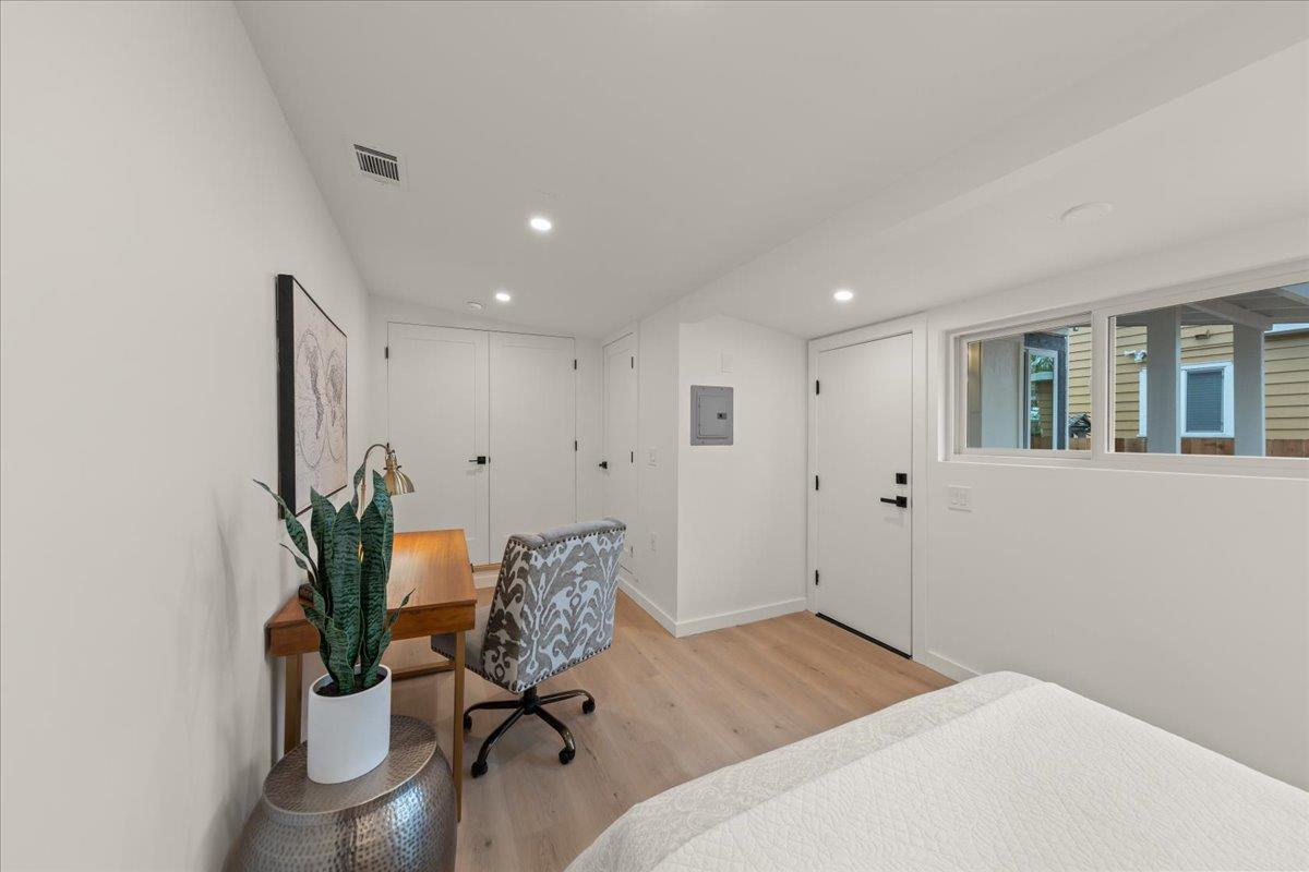 Bedroom with light wood floors, a desk and chair, and a wide window beside the bed.