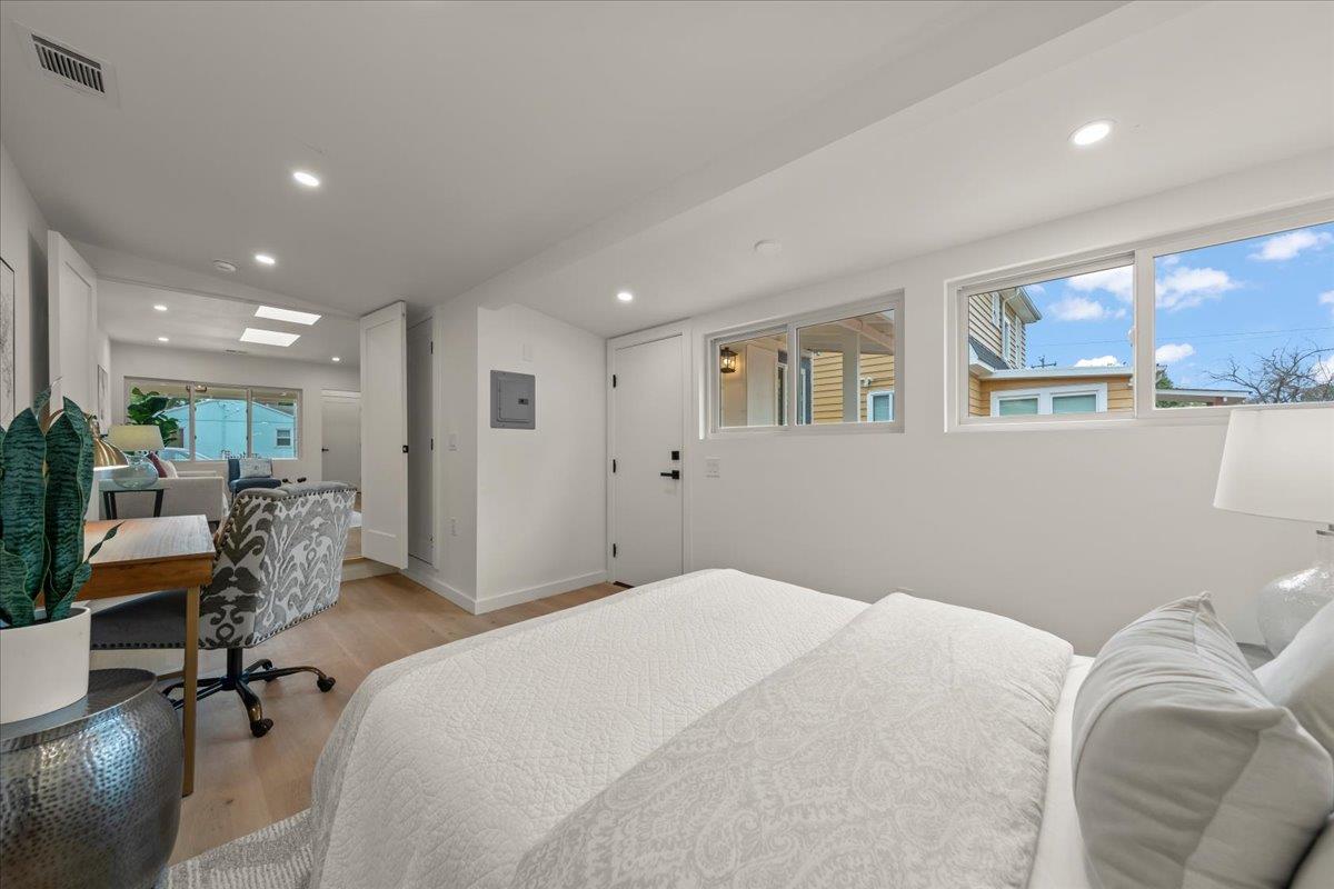 Bedroom with a white bed, desk, and windows overlooking neighboring homes.