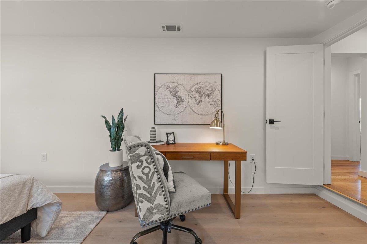 Bedroom with a wooden desk, patterned chair, framed world map, and part of a bed.