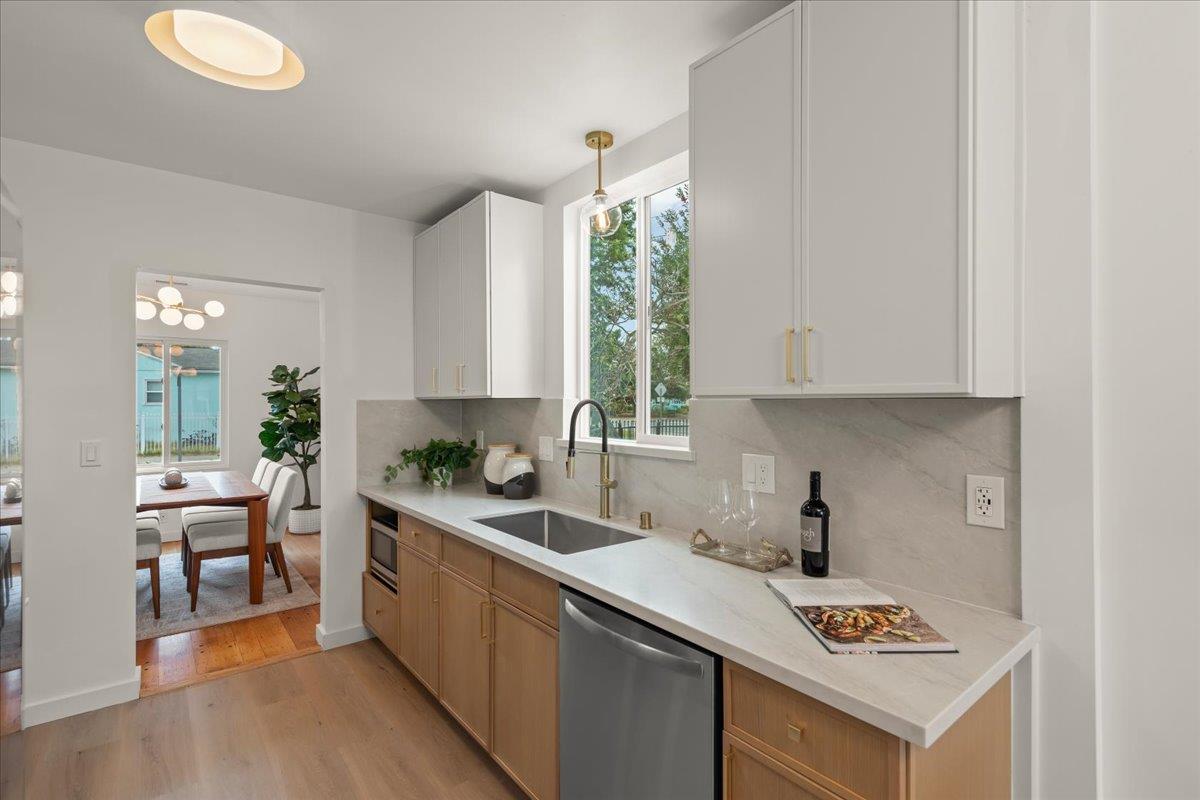 Staged kitchen with light wood cabinets, a long white counter, and a sink beneath a large window.