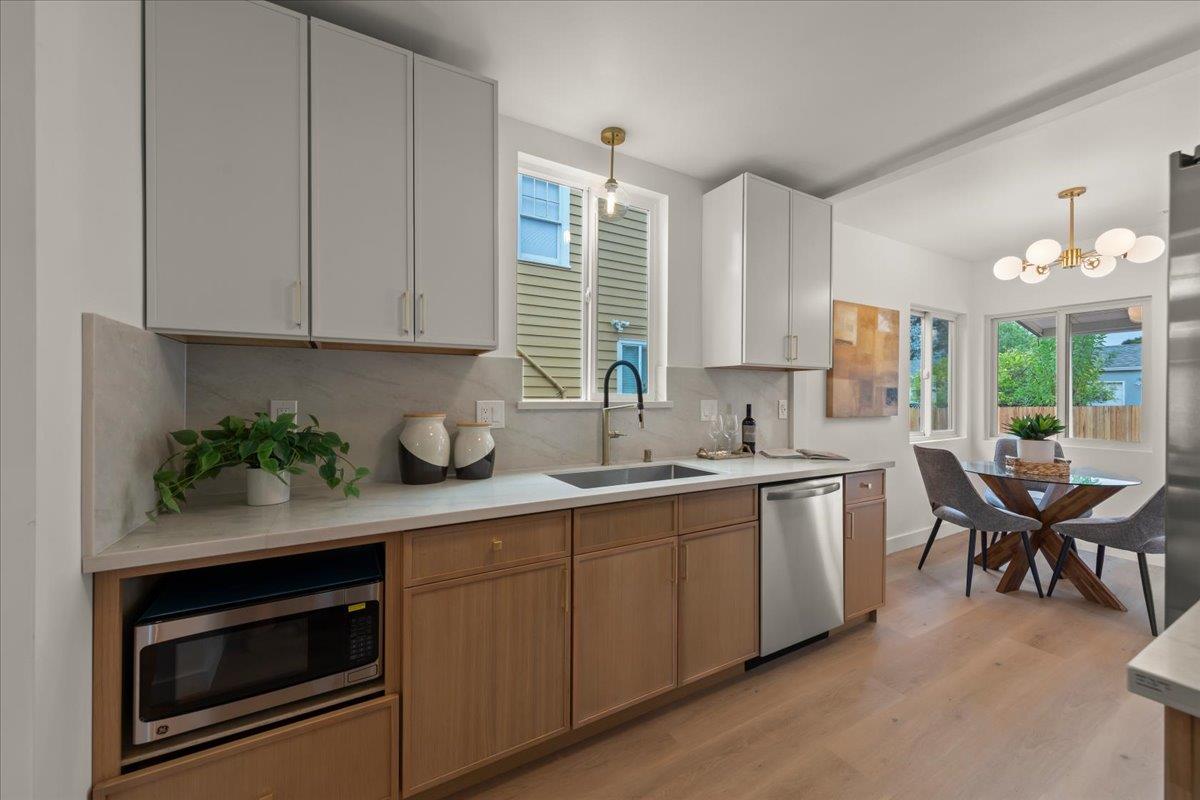 Modern kitchen with wood lower cabinets, a window above the sink, and an adjoining dining area.