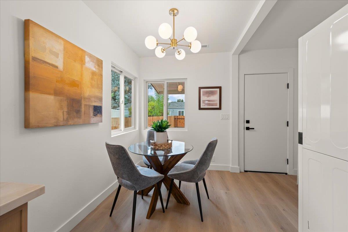 Dining area with a glass table, gray chairs, brass chandelier, and large abstract wall art.