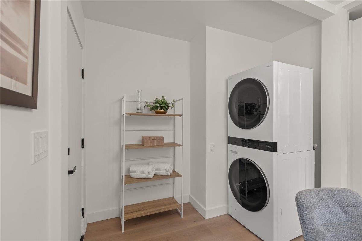 Laundry room with stacked washer and dryer beside open shelving with folded towels.