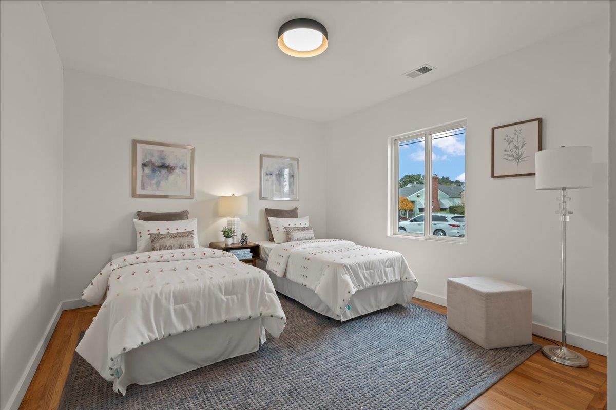 Bedroom with two twin beds, white bedding, framed art, and a large blue-gray rug.