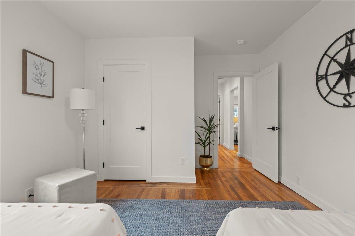 Staged bedroom with white beds, a blue rug, hardwood floors, and an open doorway.