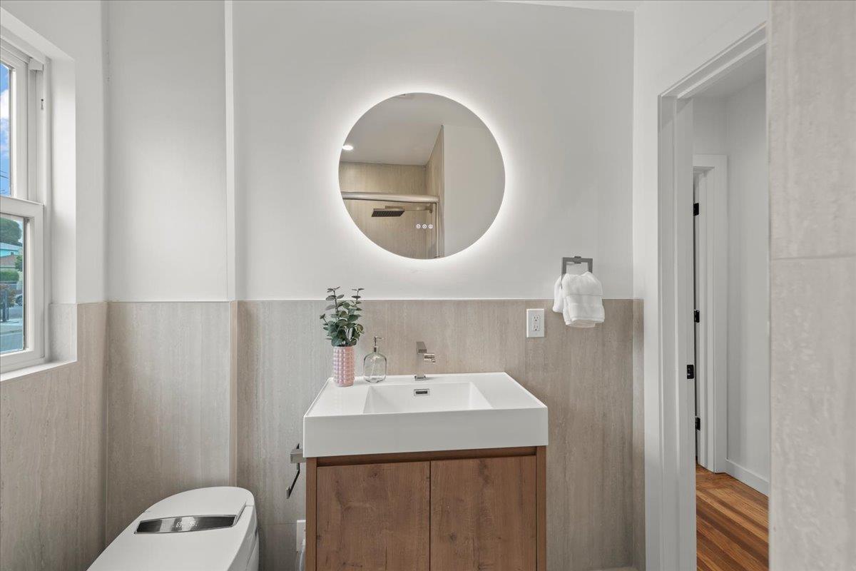Modern bathroom with a wood-front vanity, white sink, and round illuminated mirror.