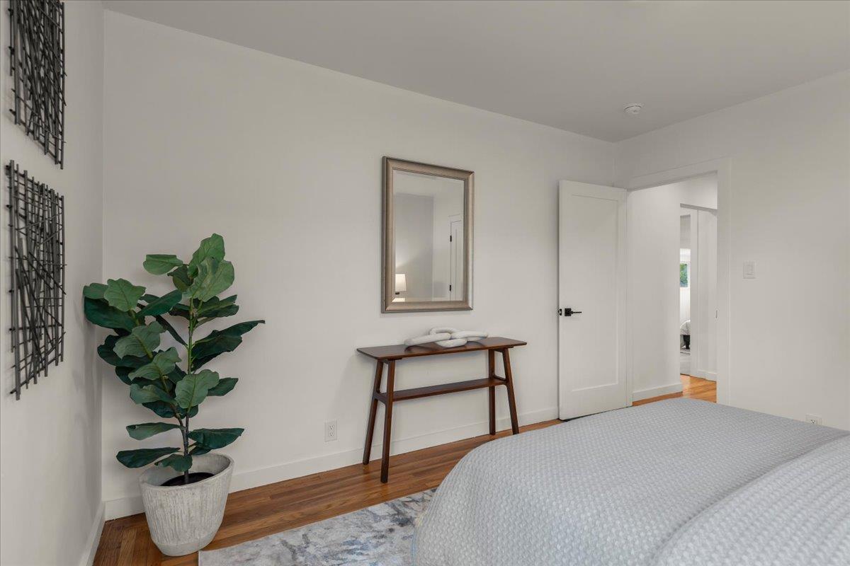 Staged bedroom with a fiddle-leaf fig, console table, and mirror beside an open doorway.