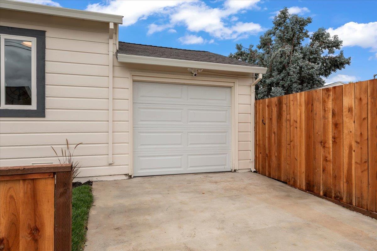 House exterior with a white garage door, concrete driveway, and tall wooden fence.