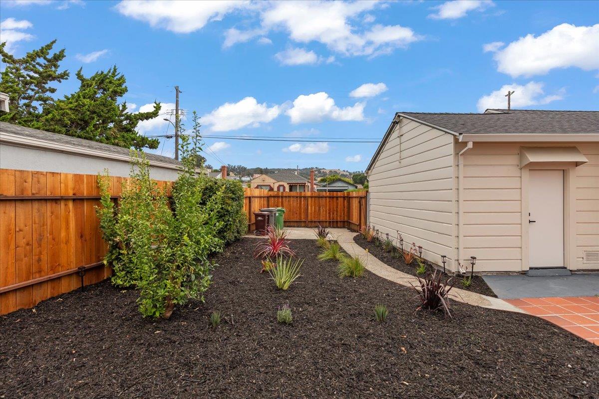 Oakland backyard with a beige outbuilding, curved path, landscaped beds, and wooden fencing.