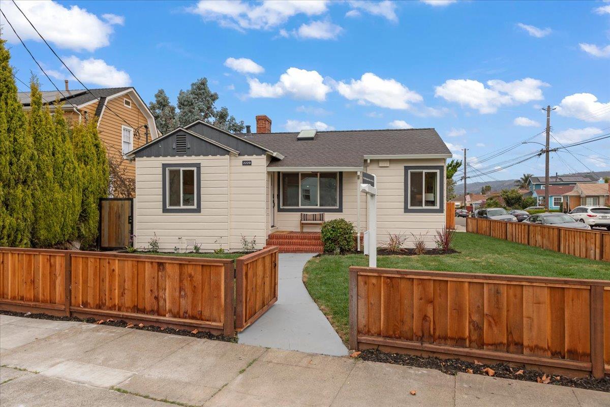 Single-story beige house with dark trim, a fenced front lawn, and a curved walkway.