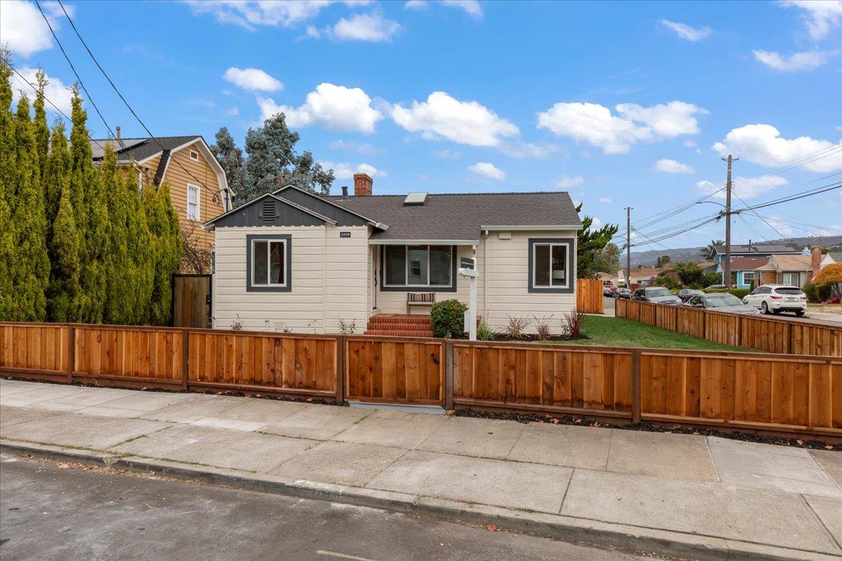 Single-story beige Oakland home behind a wooden fence, with a small front porch and dark shingle roof.