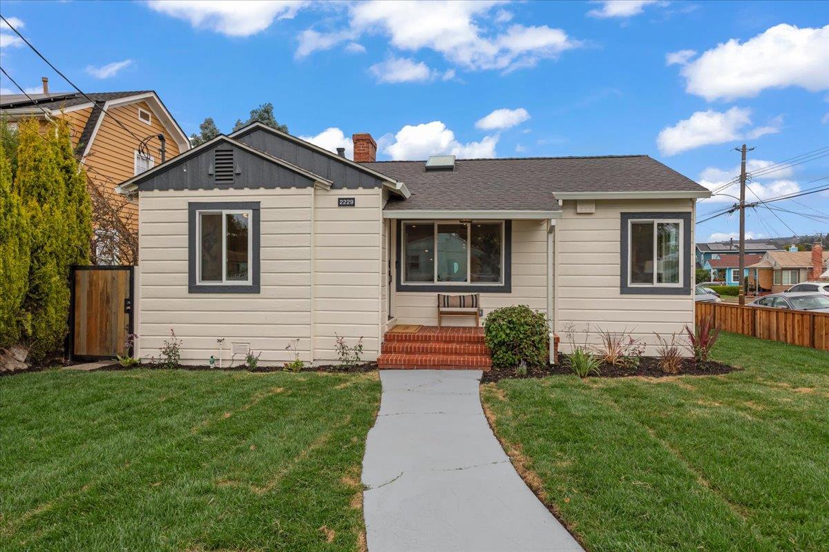 Beige single-story house with dark trim, brick front steps, and a walkway across the lawn.