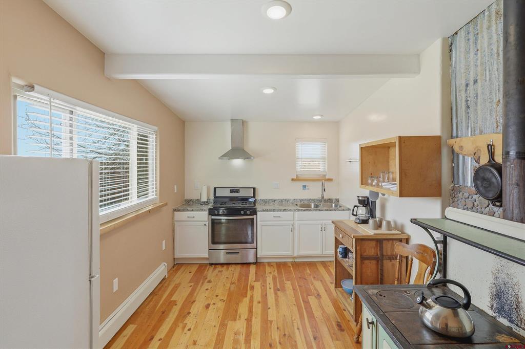 Kitchen with white cabinets, stainless steel range, wood plank flooring, and large windows.