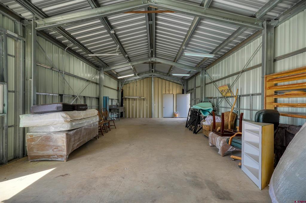 Metal outbuilding interior with a high corrugated roof and furniture stored along the sides.