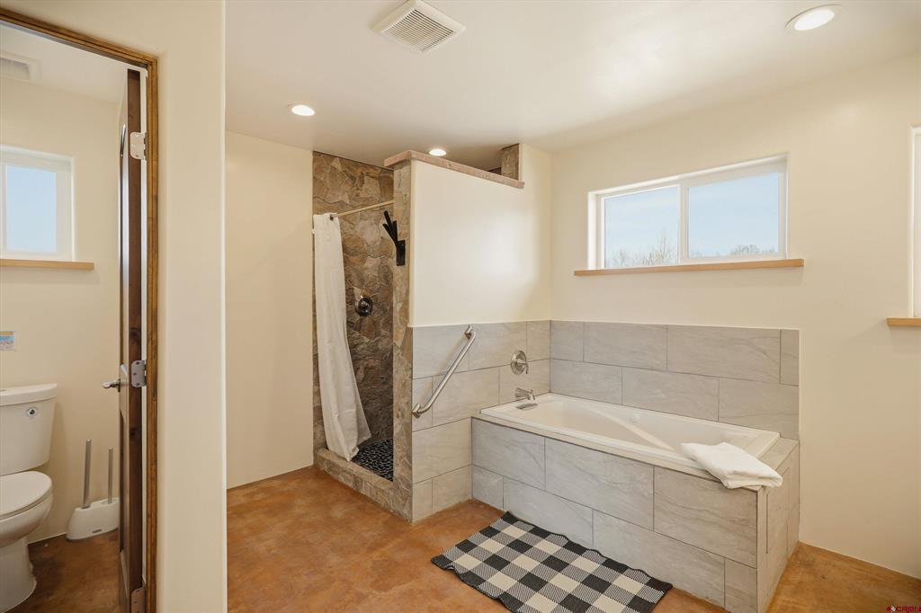 Bathroom with a tiled bathtub, stone-accented shower, and black-and-white checkered rug.