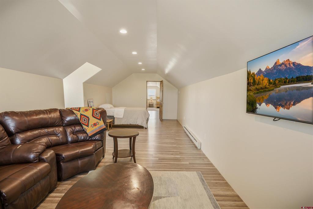 Living room with a brown leather sectional, colorful throw, and bed at the far end.