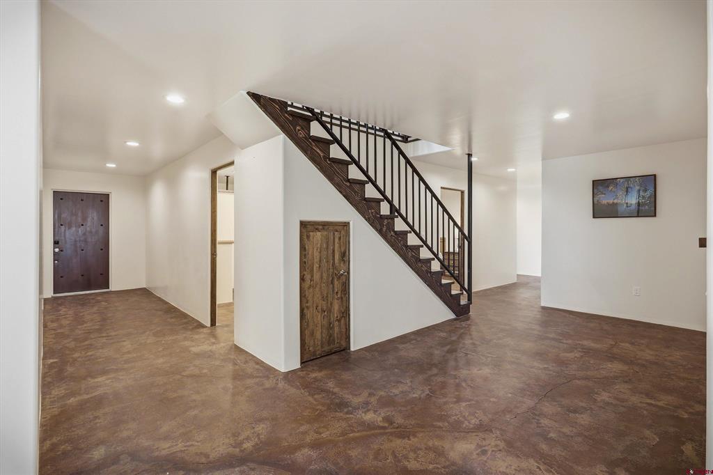 Empty home interior with a wood-and-metal staircase and mottled brown concrete floors.