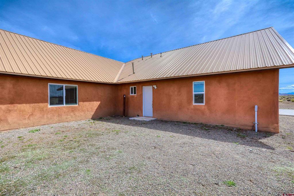 Single-story home with reddish stucco walls, a light metal roof, and a gravel yard.