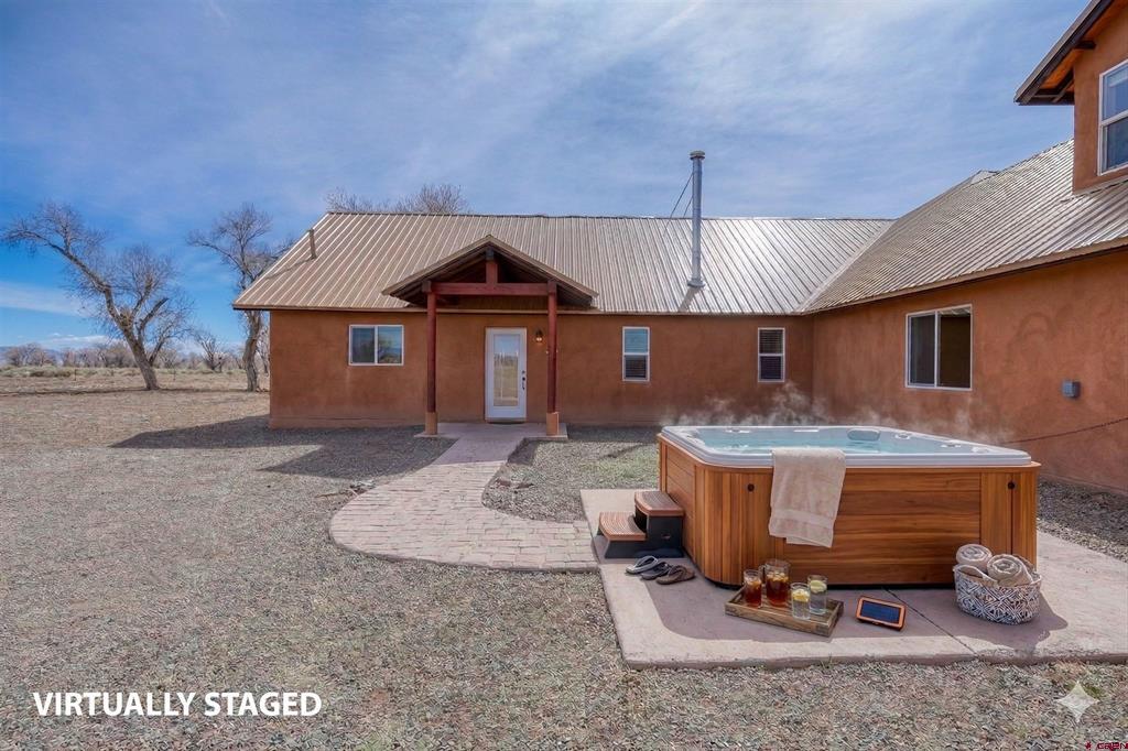 Stucco home with a metal roof, covered entry, and a hot tub on the patio.