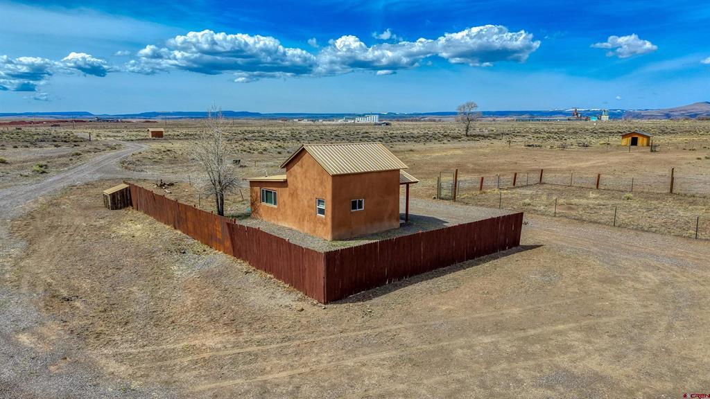 Small rust-colored home with a metal roof inside a red fenced yard on open rural land.