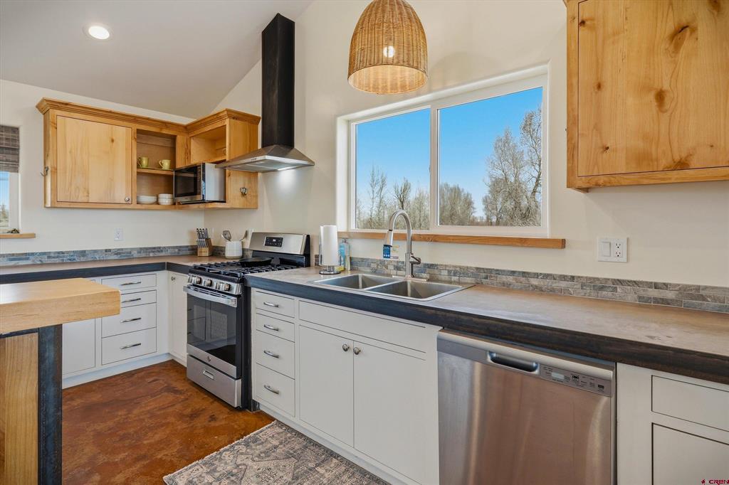 Kitchen with wood and white cabinets, dark counters, stainless appliances, and a sink beneath a large window.