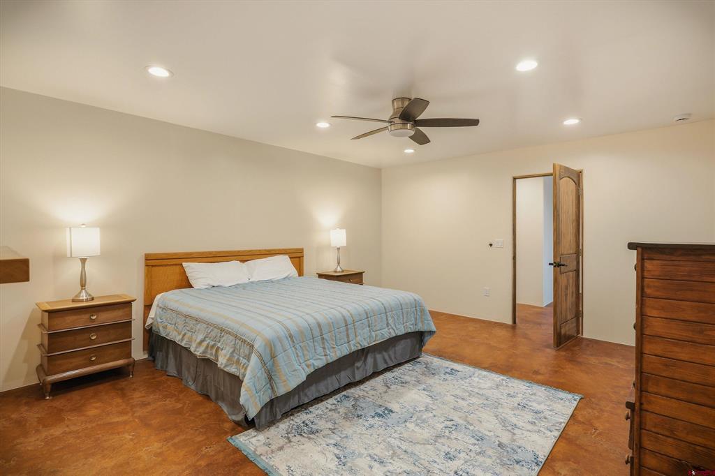 Furnished bedroom with a large bed, wooden dressers, ceiling fan, and reddish-brown flooring.