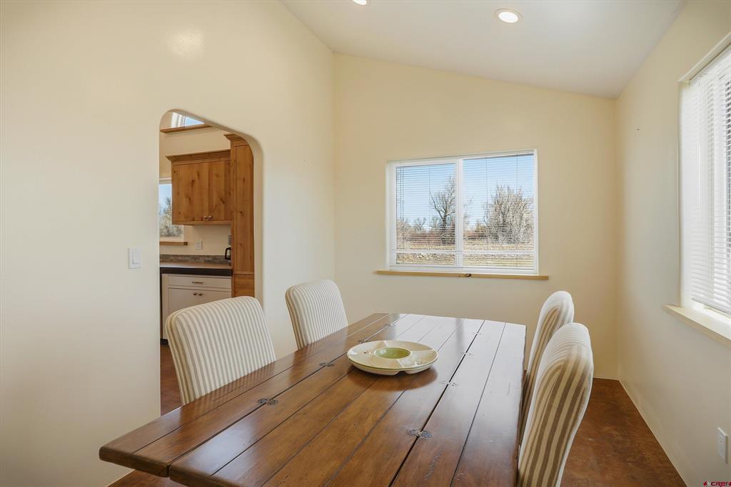 Dining room with a long wooden table, striped chairs, and an arched doorway to the kitchen.