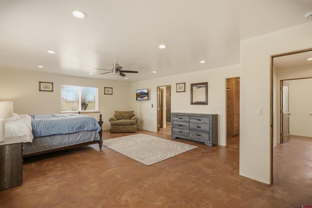 Furnished bedroom with a large bed, gray dresser, and armchair beside a window.