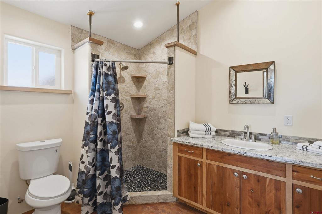 Bathroom with a stone-tiled walk-in shower, patterned curtain, and wooden vanity.
