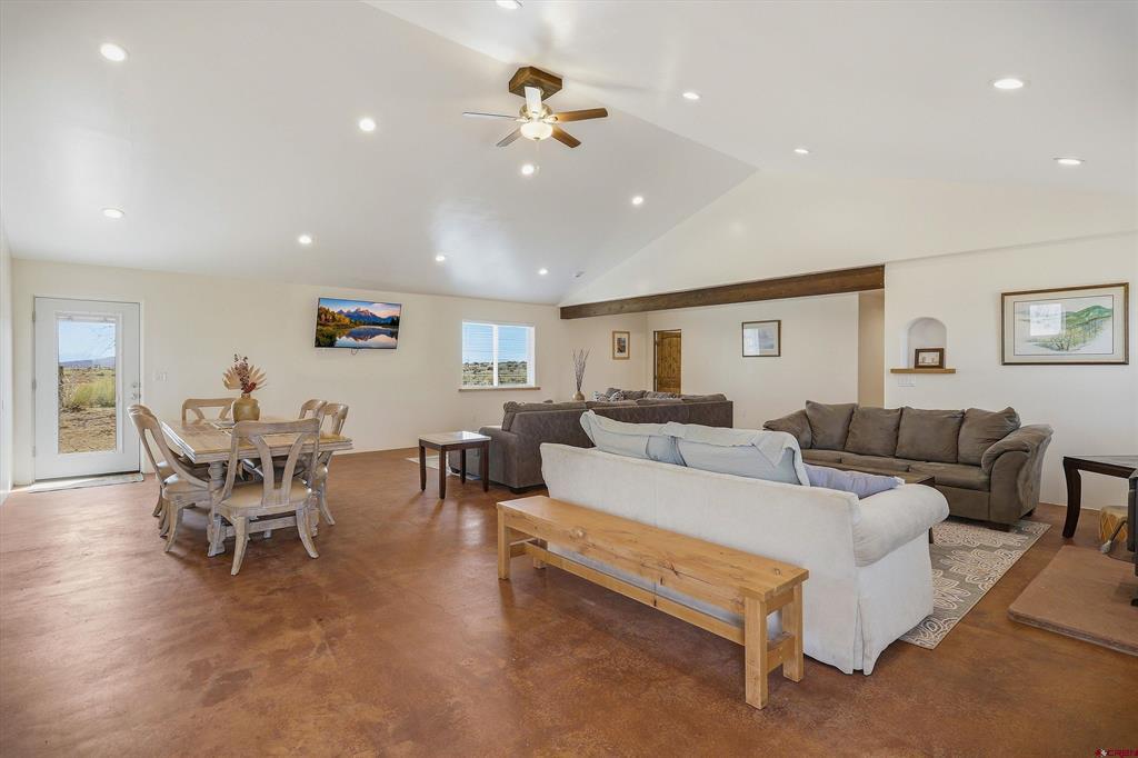 Open-plan living and dining room with vaulted ceiling, tile floors, and two seating areas.
