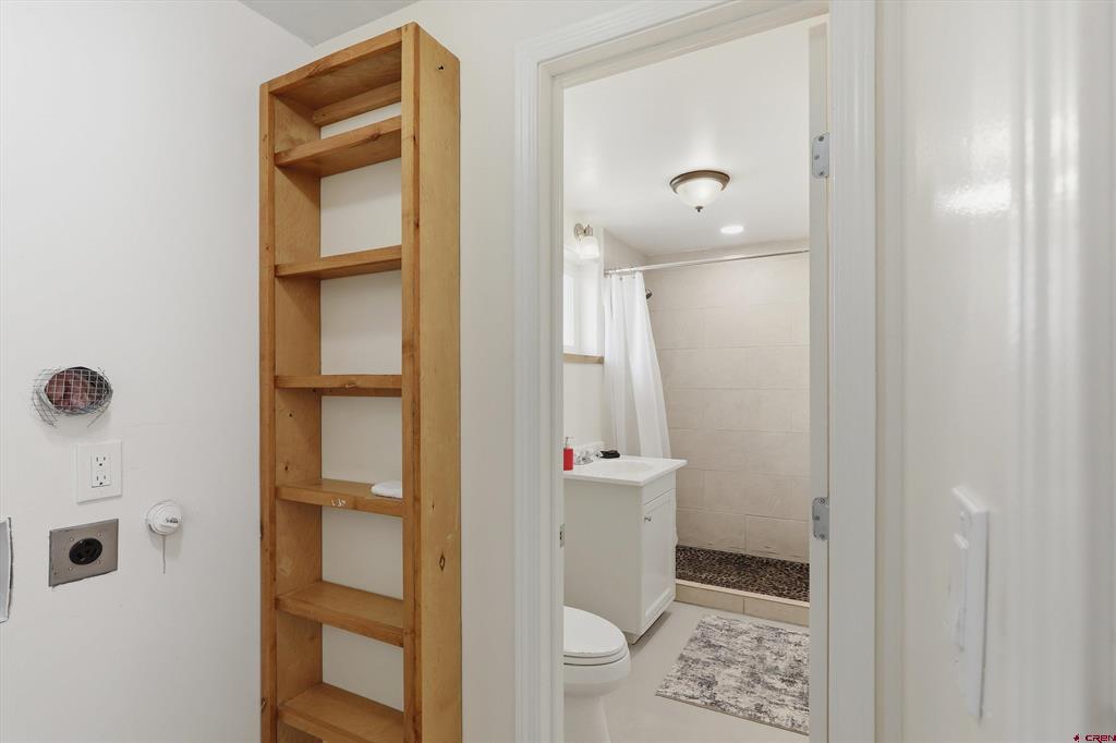 Bathroom with a tall wooden shelving unit beside a tiled shower with a pebble floor.
