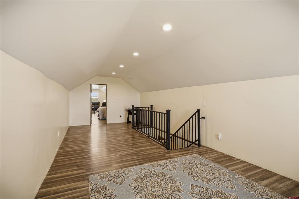 Upstairs loft landing with a black stair railing, sloped ceiling, and patterned rug.
