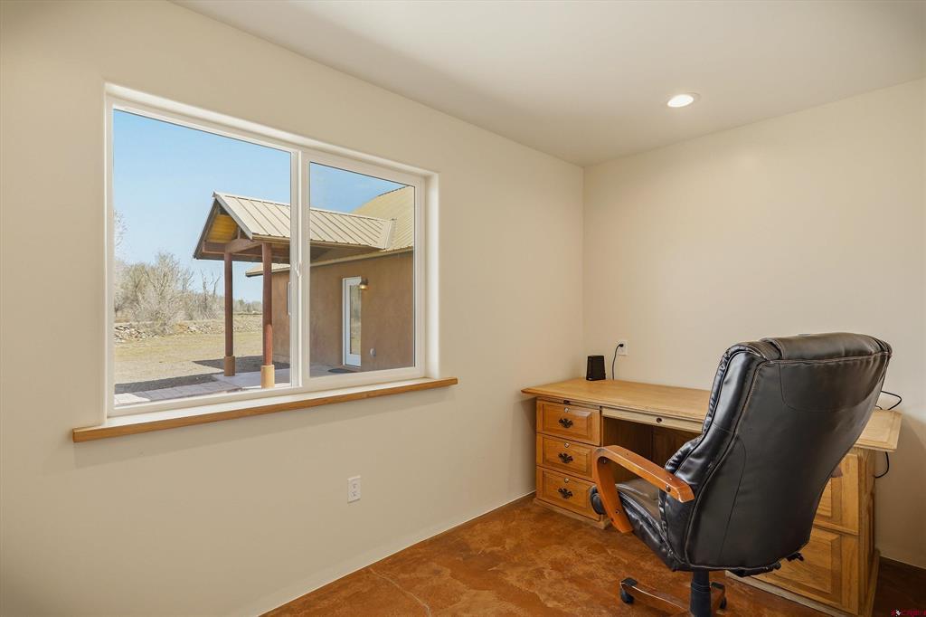 Home office with wooden desk and leather chair beside a large window overlooking a covered porch.