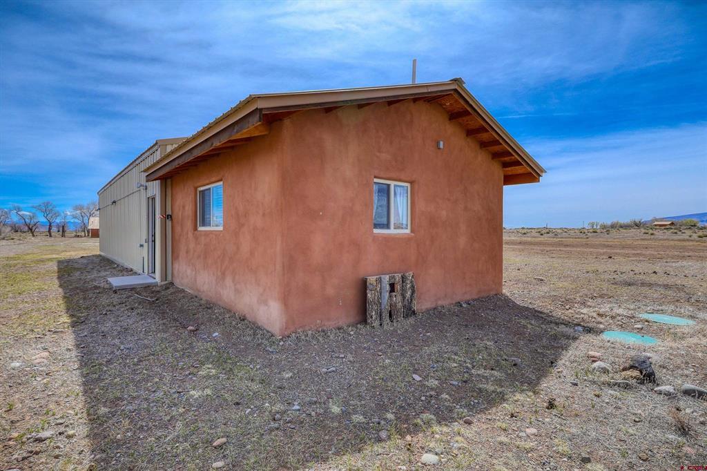 Reddish-brown stucco home with a gabled roof beside a metal outbuilding on an open rural lot.