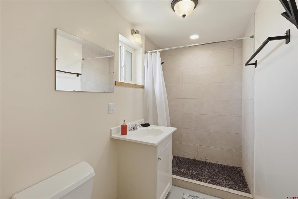 Bathroom with a tiled walk-in shower, pebble floor, white vanity, and small window.